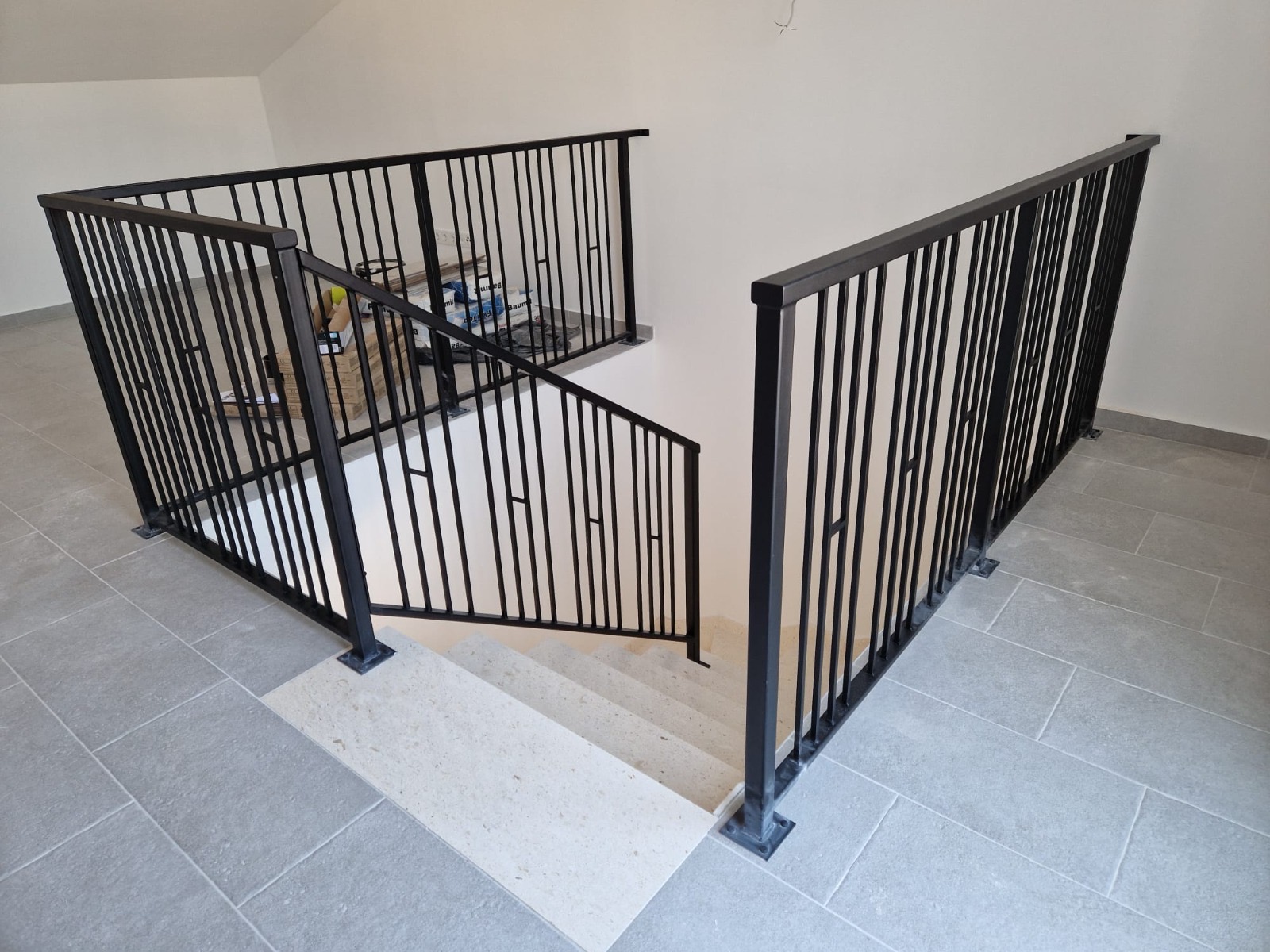 Crna metalna ograda s tankim vertikalama oko otvora stubišta na gornjoj etaži