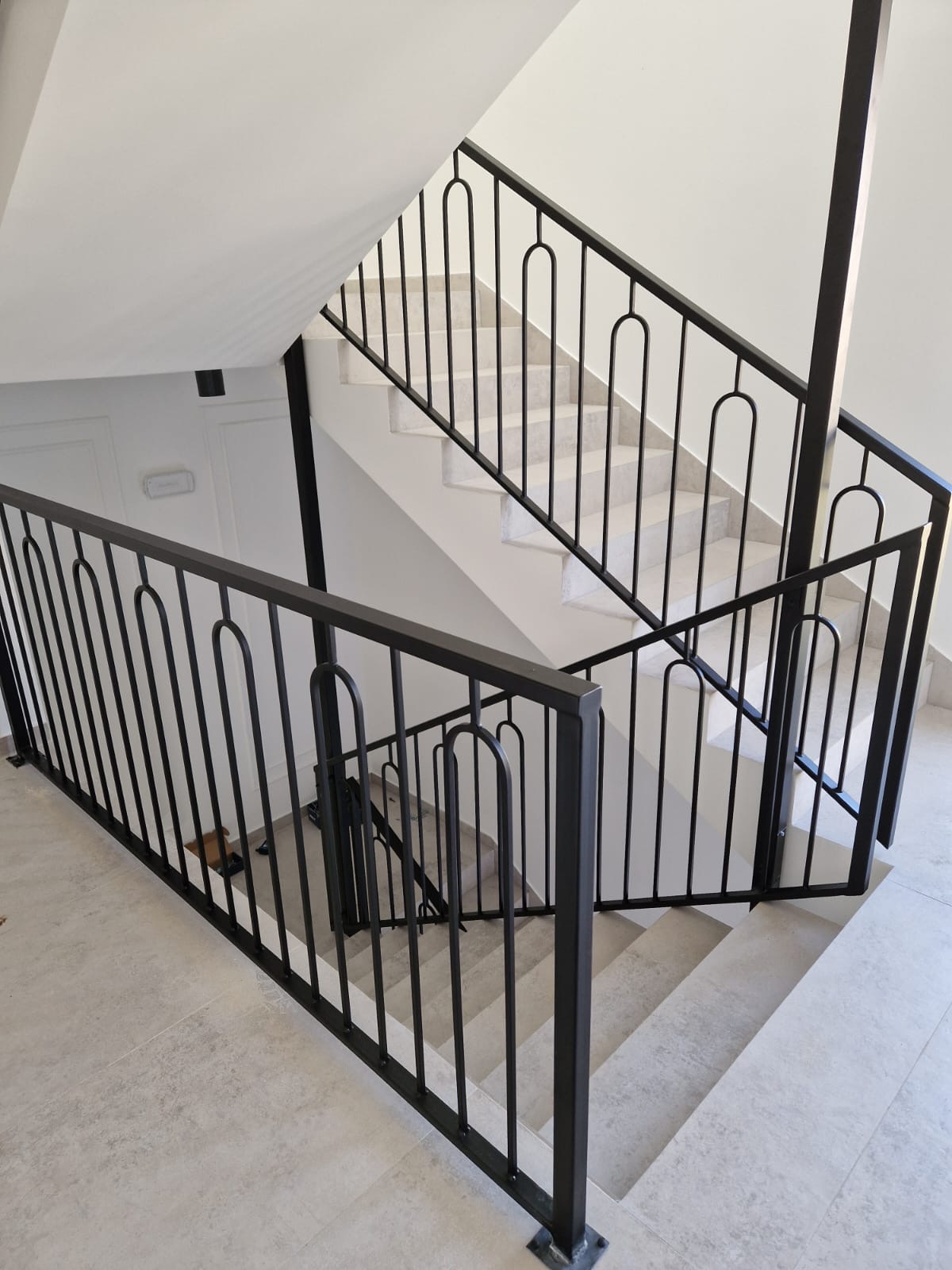Moderna crna metalna ograda s vertikalnim šipkama i zaobljenim lukovima na unutarnjem stubištu